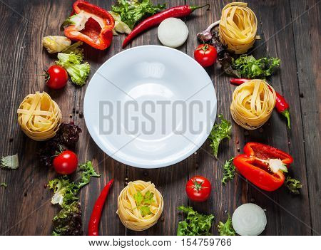 Ingredients for cooking spagetti cherry tomatoes pepper around a white plate place text frame on wooden rustic background top view.