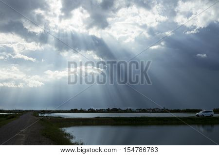 light from sun through cloud to ground, water and car