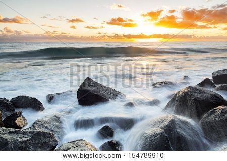 Sunrise with ocean wave and water cascading over the rocks at Burleigh Headland