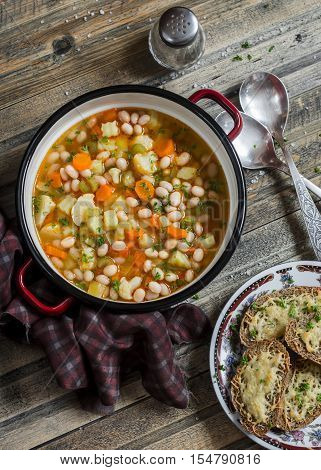 Vegetable bean soup and parmesan cheese toasts on a wooden rustic table top view. Delicious vegetarian lunch
