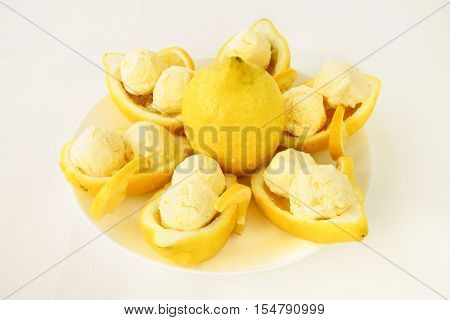 Amalfitano lemon halves filled with homemade lemon ice cream served on a white porcelain plate. An ivory colored tablecloth as background.