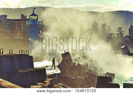 Big waves breaking over man and dog on Wollongong harbor break wall and lighthouse, Wollongong, New South Wales, Australia. Toned image