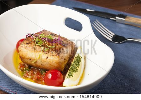 Fish steak serve with lemon and tomato in the bowl