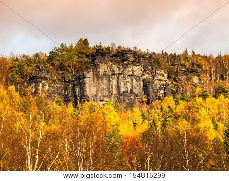 Sandstone rock formation in the middle of colorful autumn forest. Dramatic evening view. Tisa Rocks, aka Tiske Walls, Czech-Saxon Switzerland, Czech Republic