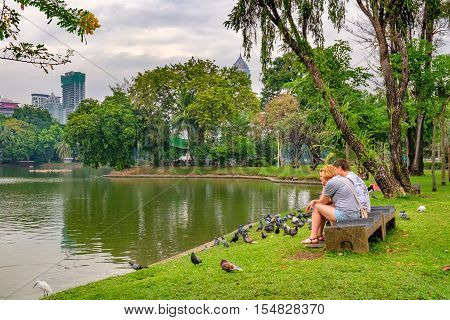 Bangkok, Thailand - December 23, 2015: Tourists couple relax and feed pigeons in a city park in the heart of Bangkok - Lumphini Park