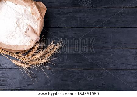 Baking background. Flour in paper bag and wheat on dark wooden table. Ingredients for cooking. Top view. Copy space