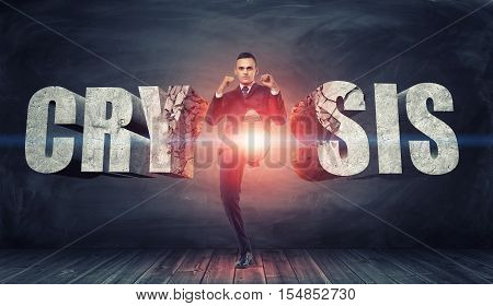 Businessman kicks and destroys concrete letters 'Crisis' with confident face expression. To overcome the crisis. Do not to break down. Strength of will. Believe in yourself.