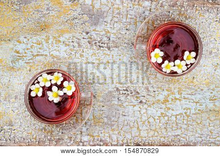 Two glass cups of tea on old wooden surface. Small white flowers.