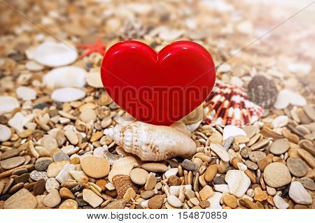 Red heart on a beach background. The pebbles sea shells and starfish.