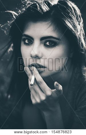 Closeup black and white portrait of white Caucasian beautiful young woman lying on ground grass smoking cigarette bad unhealthy habit lifestyle concept