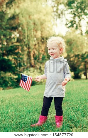 Happy adorable little blond Caucasian girl smiling laughing holding and waving American flag outside celebrating 4th july Independence Day Flag Day concept.