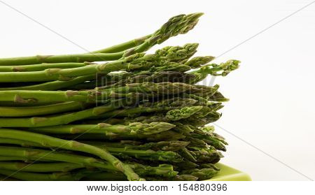 Fresh asparagus spears laid lengthwise on green plate against white background with copy space on right of horizontal photograph.