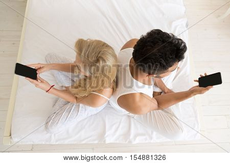 Young Couple Lying Separate In Bed, Serious Upset Hispanic Man And Woman Using Cell Smart Phone, Top Angle View Lovers Problem Conflict In Bedroom