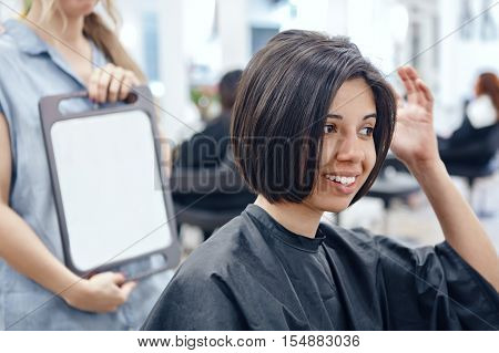 Closeup portrait of hispanic latin girl woman sitting in chair in hair salon looking in mirror at her new haircut short bob pixie happy joy emotion