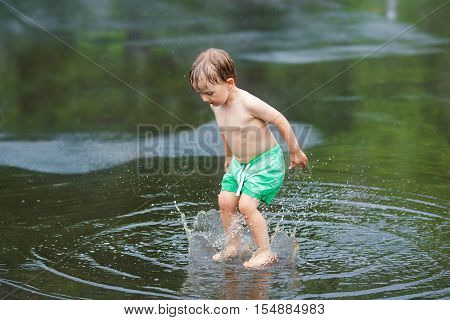 Portrait of happy toddler boy jumping in puddles during the rain thunderstorm on a bright summer day outside sports recreation leisure concept childhood and freedom