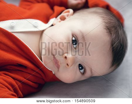 Closeup portrait of cute adorable Caucasian baby boy girl with black brown eyes in red hoodie shirt on changing table looking directly in camera natural light indoors
