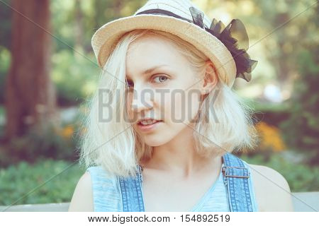 Portrait of beautiful Caucasian teenage young blonde alternative model girl woman with light grey blue eyes in straw hat with bow looking in camera toned with Instagram filters