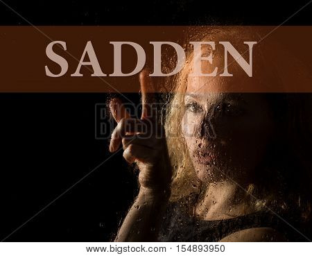 sadden written on virtual screen. hand of young woman melancholy and sad at the window in the rain