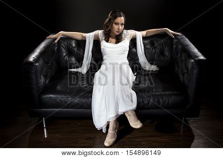Bridal modeling modern fashion trend of simple but elegant thin wedding dress in retro or art deco style. Bride on couch with shoulder scarf and bridal gown.