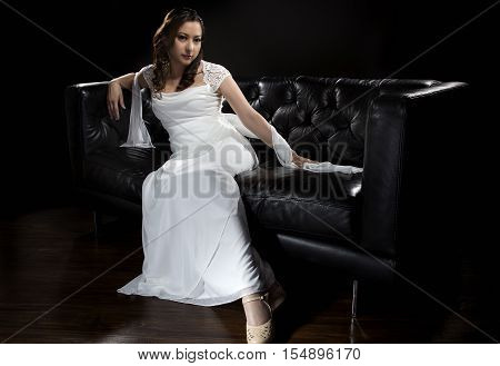 Bridal modeling modern fashion trend of simple but elegant thin wedding dress in retro or art deco style. Bride on couch with shoulder scarf and bridal gown.