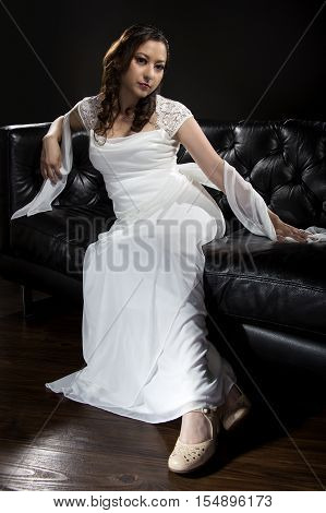 Bridal modeling modern fashion trend of simple but elegant thin wedding dress in retro or art deco style. Bride on couch with shoulder scarf and bridal gown.