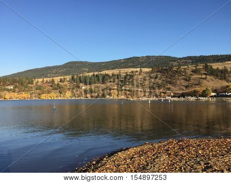 Blue sky and calm lake with dock and hills in background.