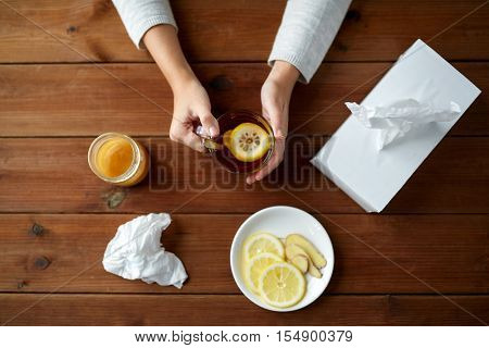 health, traditional medicine and ethnoscience concept - ill woman drinking tea with lemon, honey and ginger and paper wipes box on wooden table