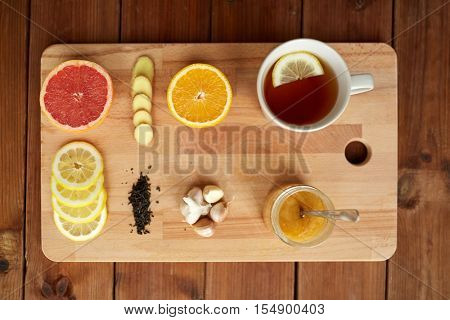 health, traditional medicine, folk remedy and ethnoscience concept - cup of ginger tea with honey, citrus and garlic on wooden board