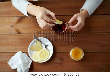health, traditional medicine and ethnoscience concept - close up of woman adding lemon to tea cup
