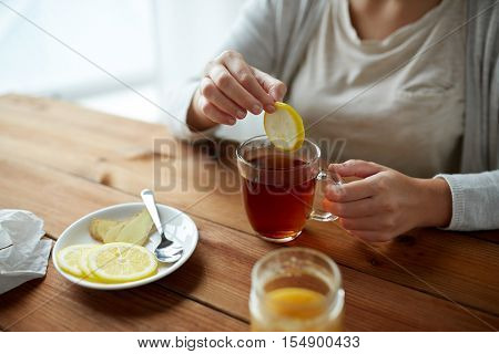 health, traditional medicine and ethnoscience concept - close up of woman adding lemon to tea cup