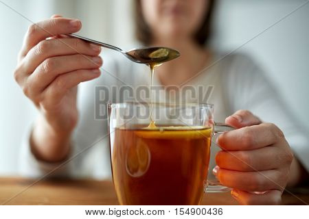 healthy food, eating and ethnoscience concept - close up of woman adding honey to tea cup with lemon
