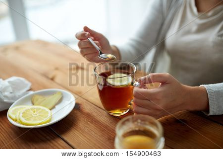 healthy food, eating and ethnoscience concept - close up of woman adding honey to tea cup with lemon and ginger
