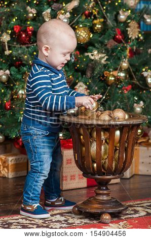 The child stays on the floor near the New year tree and tuchs the new year's toys