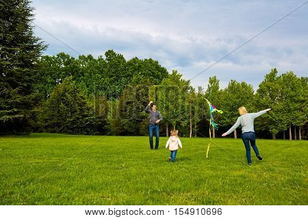 Happy Young Family With Flying A Kite In The Park.