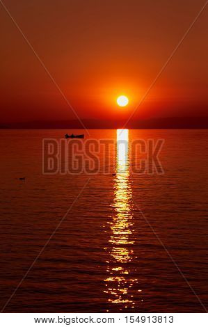 Beautiful red sunset at the sea. Big red sun over the sea. Silhouette of a fisherman in a boat on the surface of the sea sea gulls adorn the landscape.