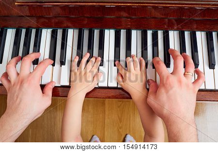 Top view close-up of hands of father and child on a piano keyboard. The parent teaches the kid to play the piano. The concept of education children's education.