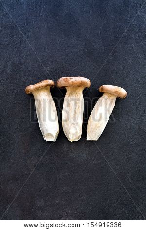 Three king oyster mushrooms on dark gray slate background