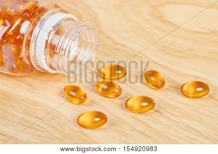 Fish oil capsules with omega 3 and vitamin D in a bottle on wooden texture healthy diet conceptclose up shot.