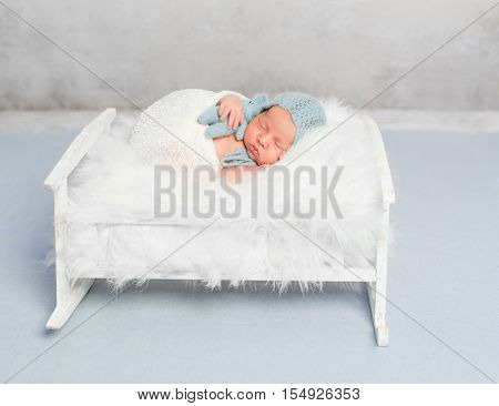 dreamy newborn boy holding toy sleeps on little bed covered with white fluffy blanket