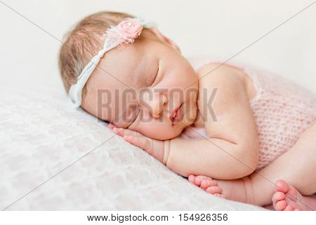 sweet face of a newborn girl with headband and flower on head sleeping on hand, close up