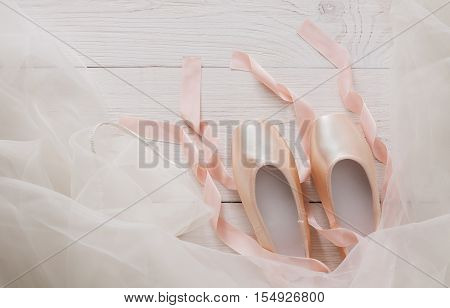 Pastel pink ballet shoes background. New pointe shoes with satin ribbon and chiffon tutu lay on white rustic shubby chic wood, top view with copy space