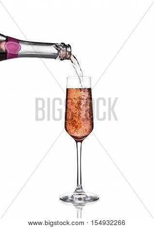 Pouring pink rose champagne from bottle to glass on white background with reflection