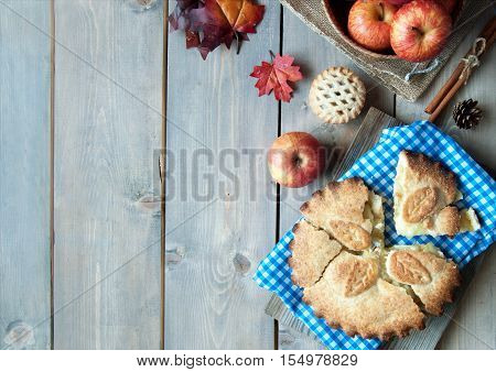 Apple pie with fruit ingredients autumn leaves and cinammon sticks on a wooden table