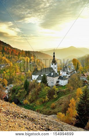 Fall in Slovakia. Old mining village. Historic church in Spania dolina. Autumn colored trees at sunset.