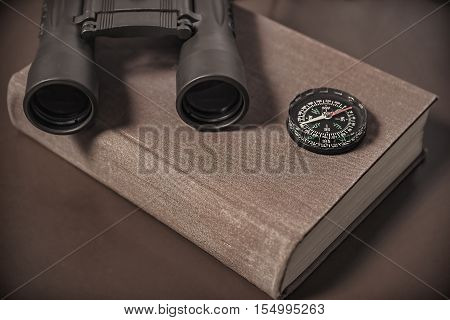 Binoculars compass and book. Brown monochrome color.
