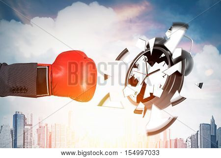 Businessman's hand in red boxing glove is smashing giant alarm clock against cityscape background. Concept of deadline. Toned image