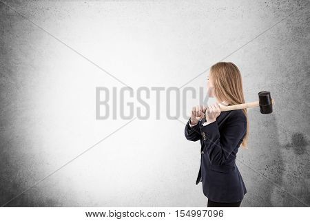Side view of blond woman with sledgehammer about to smash concrete wall. Concept of no limits. Mock up