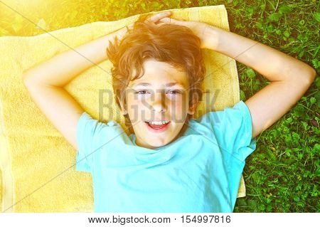Smiling boy with arms under head lay under the sun on the green grass and yellow towerl