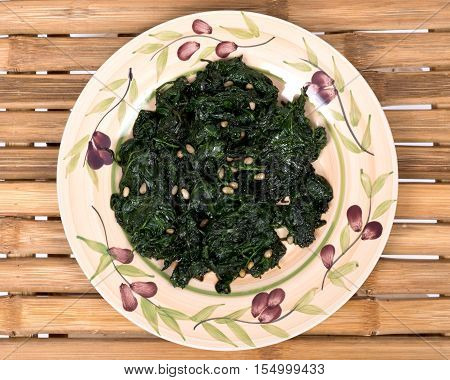 Sauteed fresh organic baby spinach with raw pine nuts on ceramic plate and bamboo table