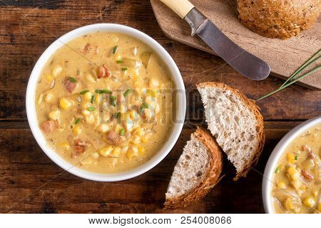 A Bowl Of Delicious Homemade Bacon Corn Chowder With Whole Grain Bread On A Rustic Wood Table Top.